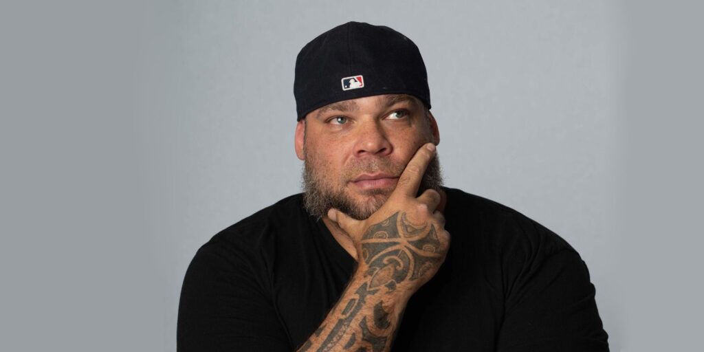 A man with tattoos and a cap is posing for the camera.